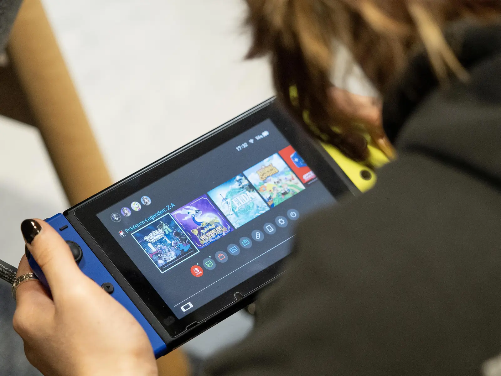 Een persoon houdt een Nintendo Switch vast waarop het menu met spellen te zien is, waaronder The Legend of Zelda.